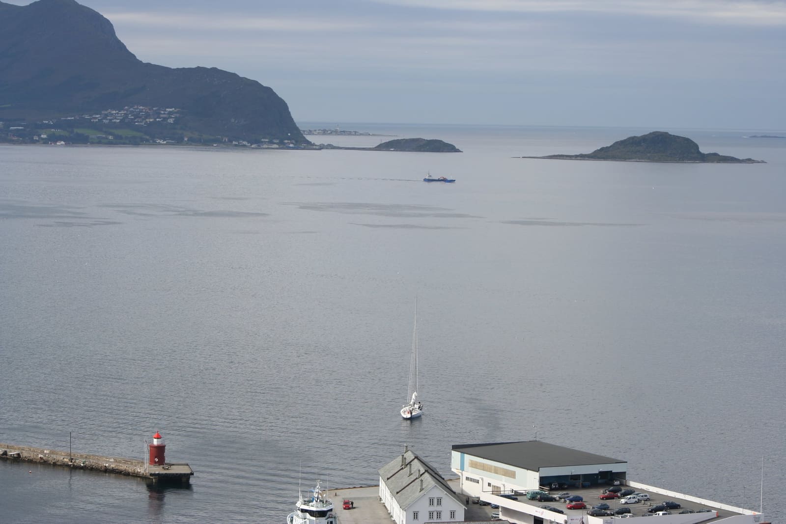 Grey, calm sea off Ålesund with the islands of Godøy and Havstein, a boat under way and a small lighthouse.