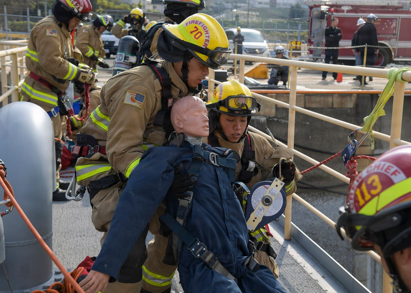 A rescue team in breathing apparatus lifts a dummy casualty out of a tank on a harness during a drill.