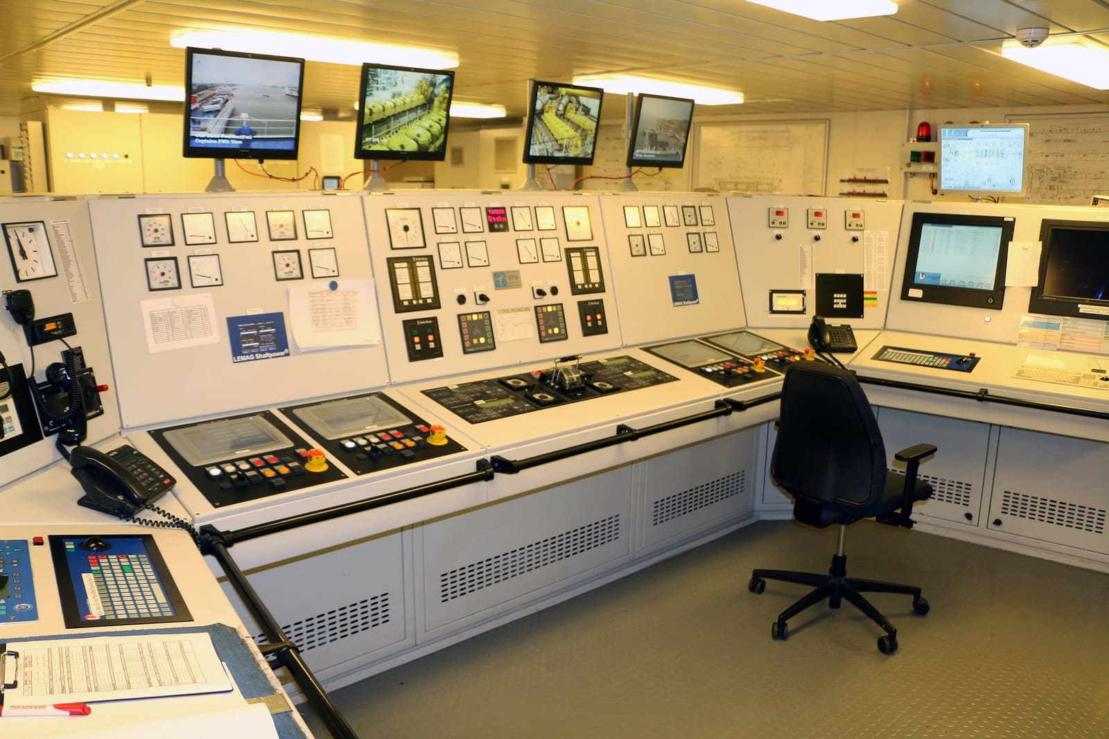 An engine control room: consoles of gauges, switches and screens, and monitors showing the engines.