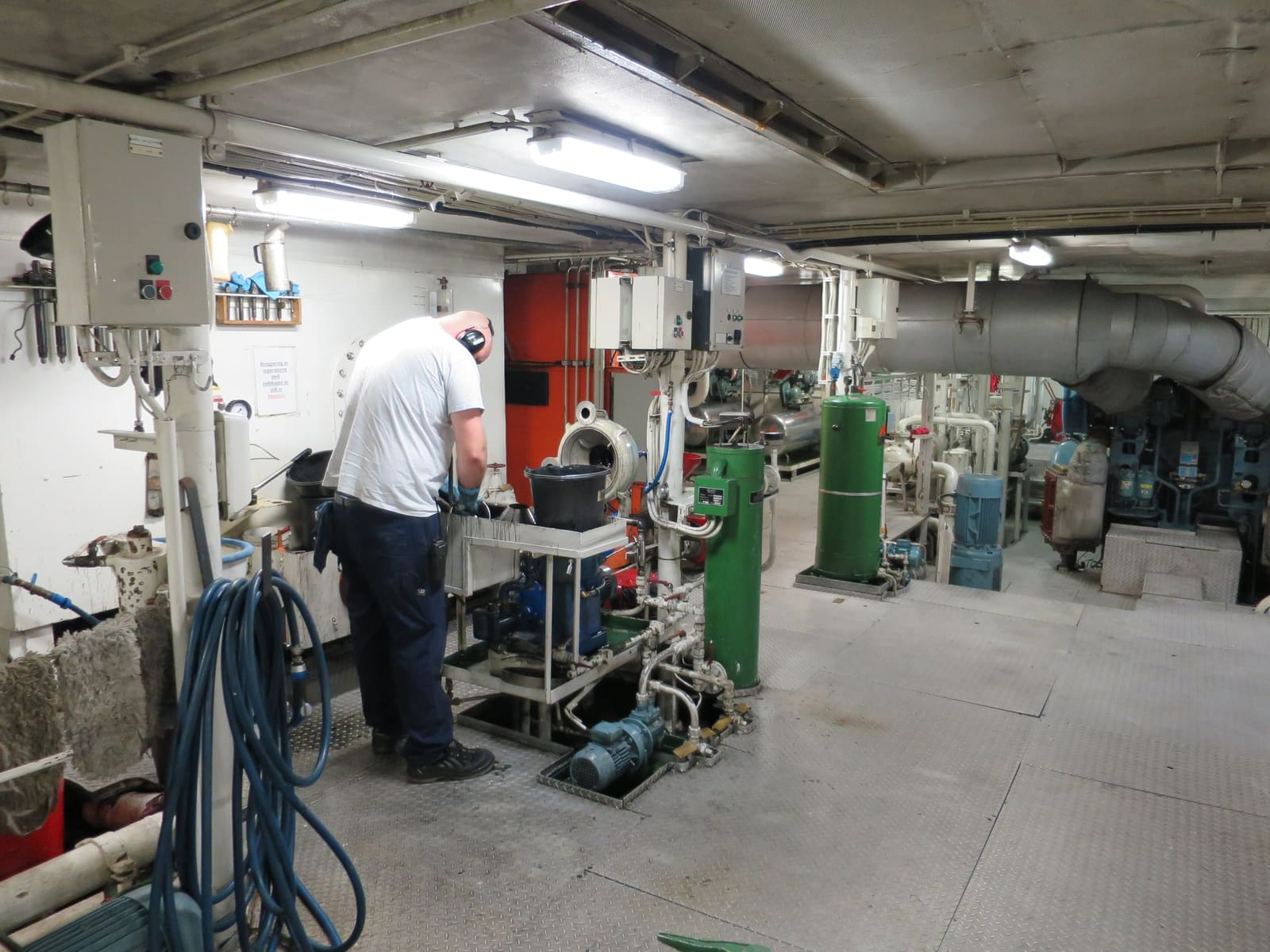An engineer working at a separator in an engine room, among pumps, tanks and hoses.