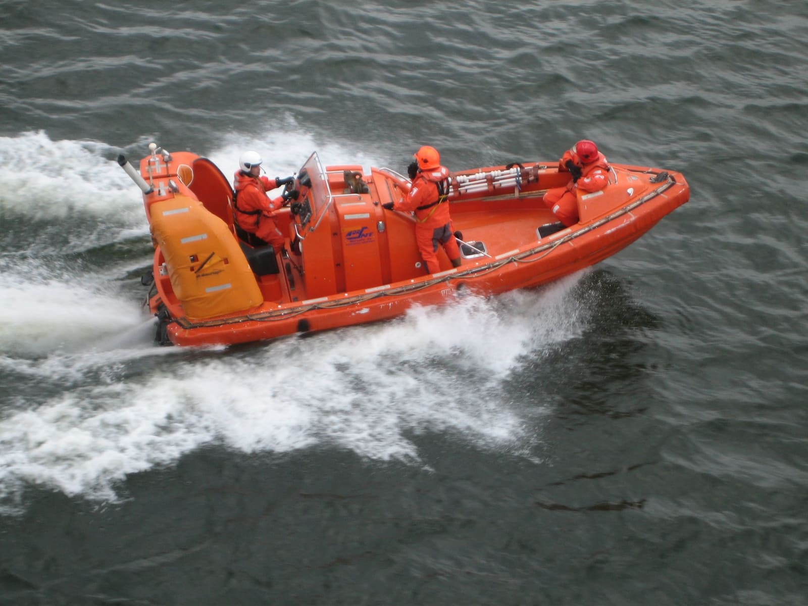 A fast rescue boat under way at speed, its crew in orange survival suits and helmets.