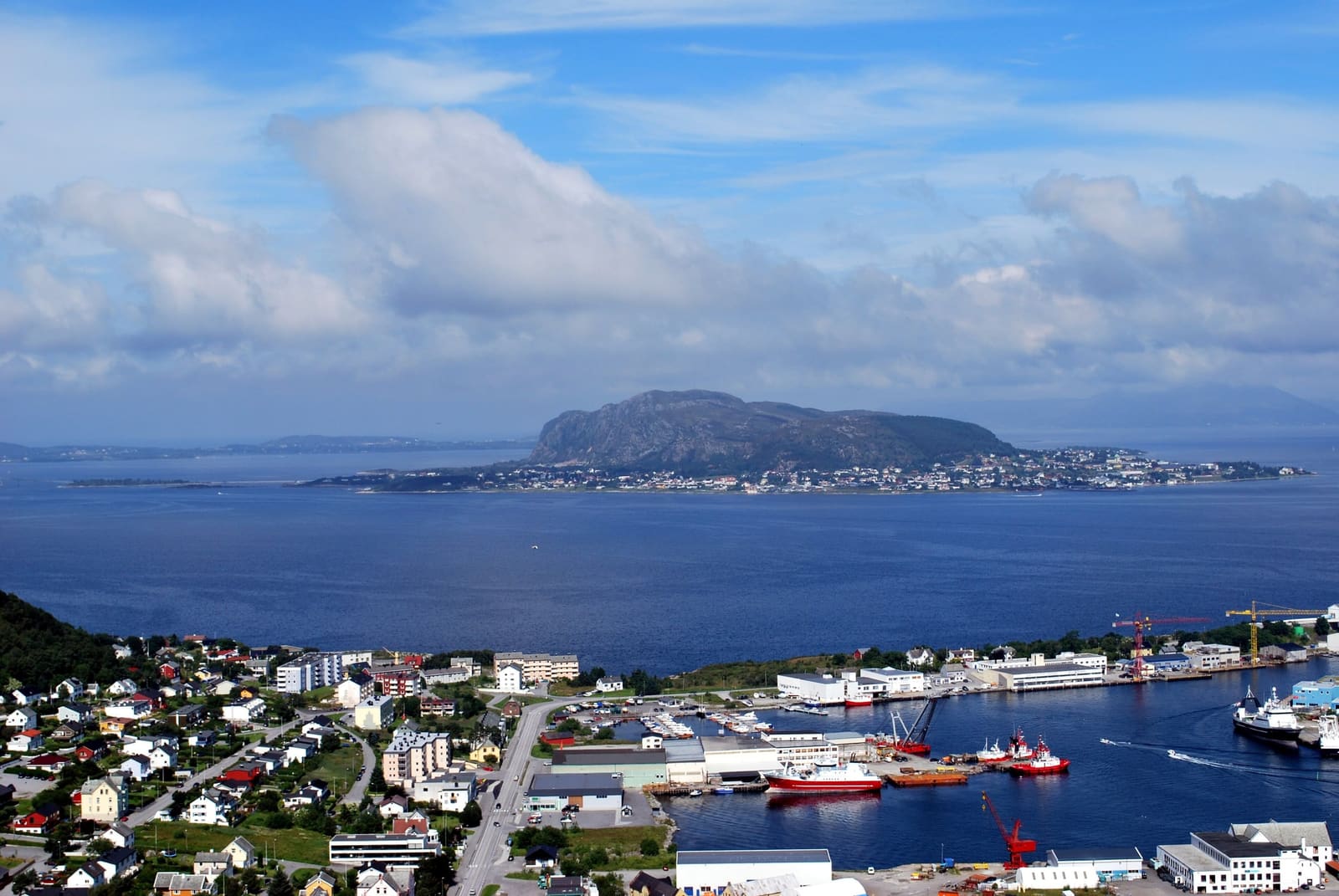 The coast outside Ålesund from above: houses and a harbour on Valderøya, and Godøya rising from the sea behind.