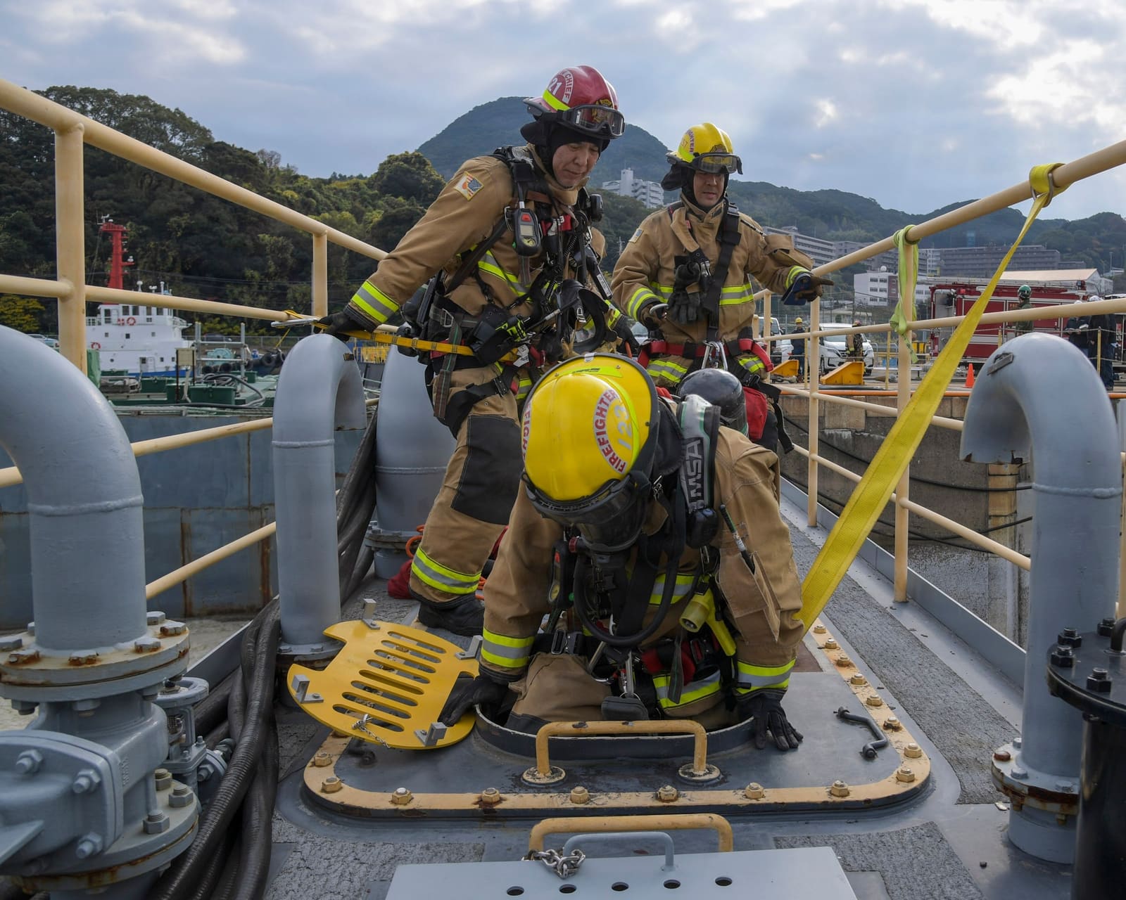 Firefighters in breathing apparatus lower themselves through a tank manhole during an enclosed space rescue drill.