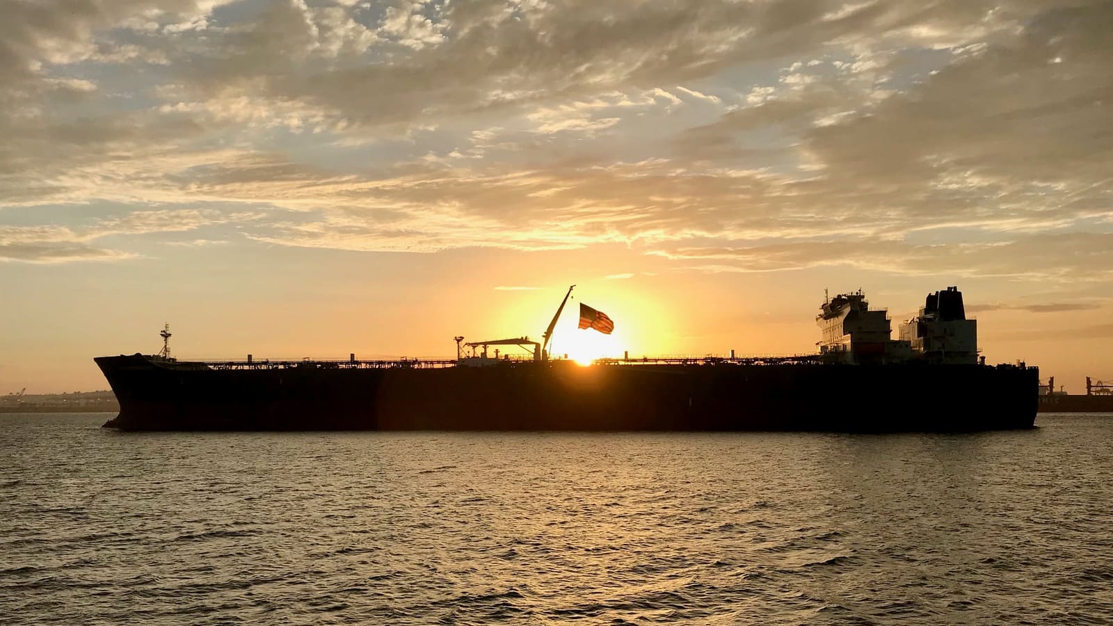 A tanker silhouetted against a low sun and a golden sky, lying in calm water.